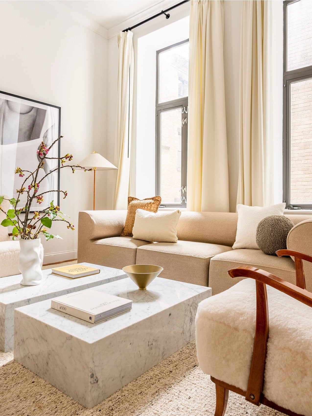 Bright living room with beige upholstered sofa, cream curtains, marble coffee tables, textured cushions and decorative vase