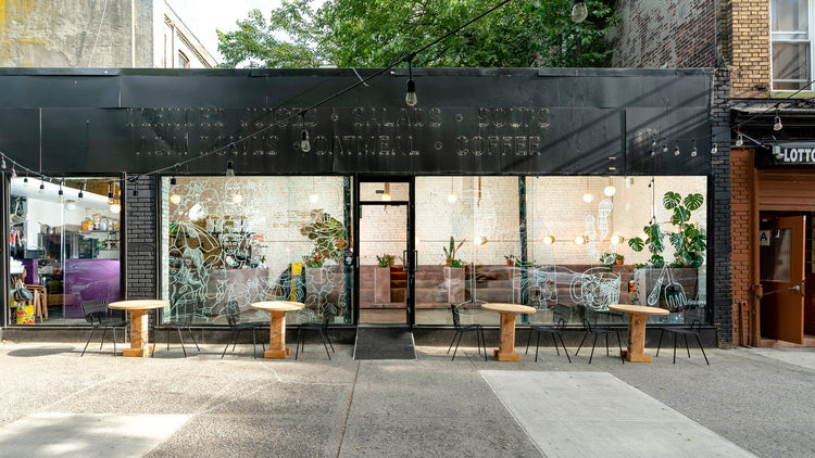Cafe storefront with black facade, large glass windows with white line art, wooden round tables and black metal chairs