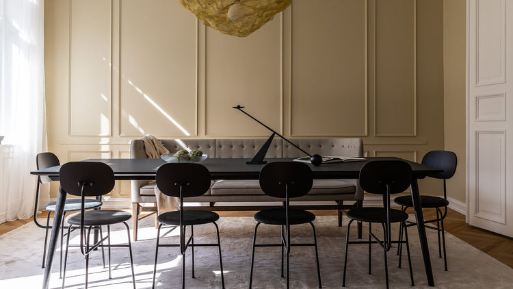 Minimalist black dining table with six black metal chairs, beige tufted bench, sculptural black table lamp and glass bowl on