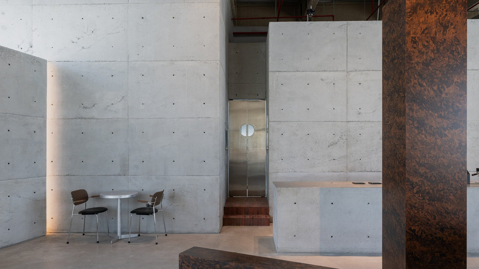 Minimal concrete interior with gray cast‑concrete walls, stainless steel door with round window, small round table and two