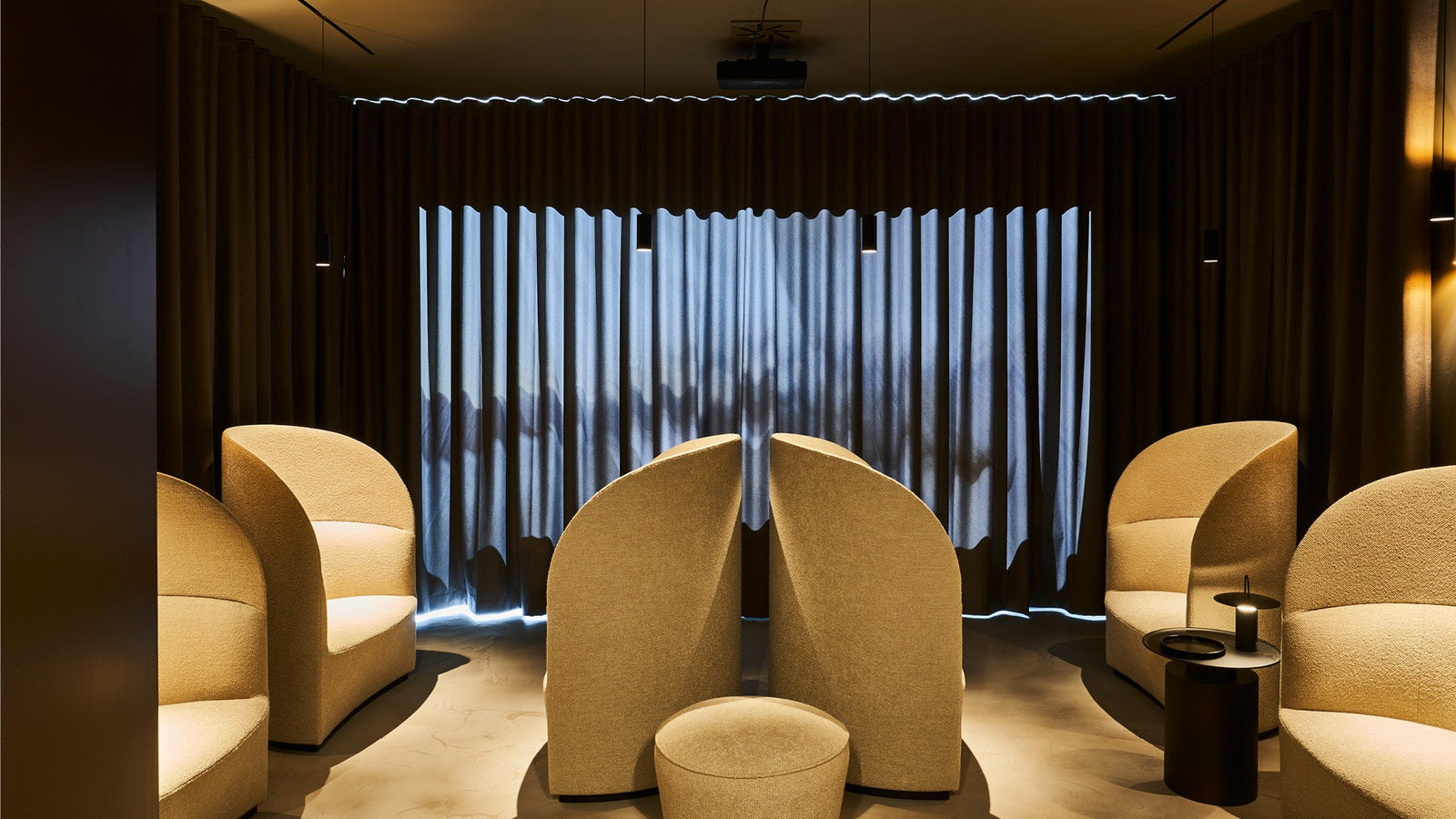 Minimalist lounge with curved beige boucle armchairs and ottoman facing floor-to-ceiling dark pleated curtains and pendant