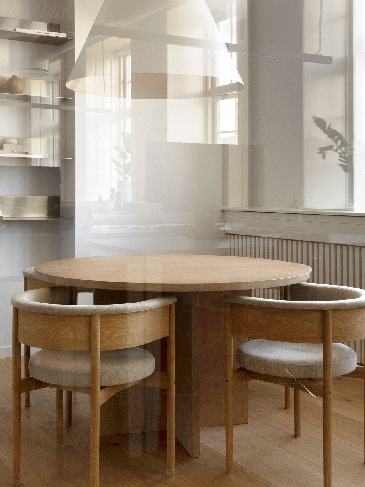 Round oak dining table with four curved oak chairs upholstered in light grey, pendant lamp and soft natural light.