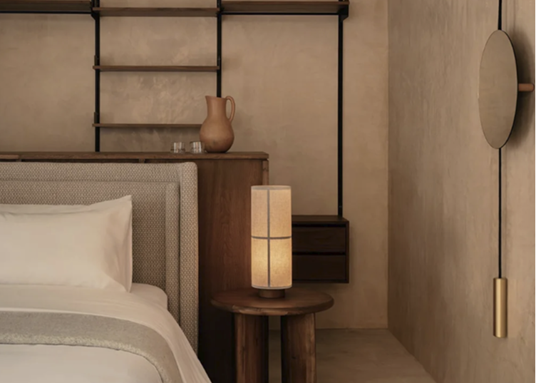 Bedside scene with beige upholstered headboard, wooden side table, round ceramic lamp with linen shade and neutral decor