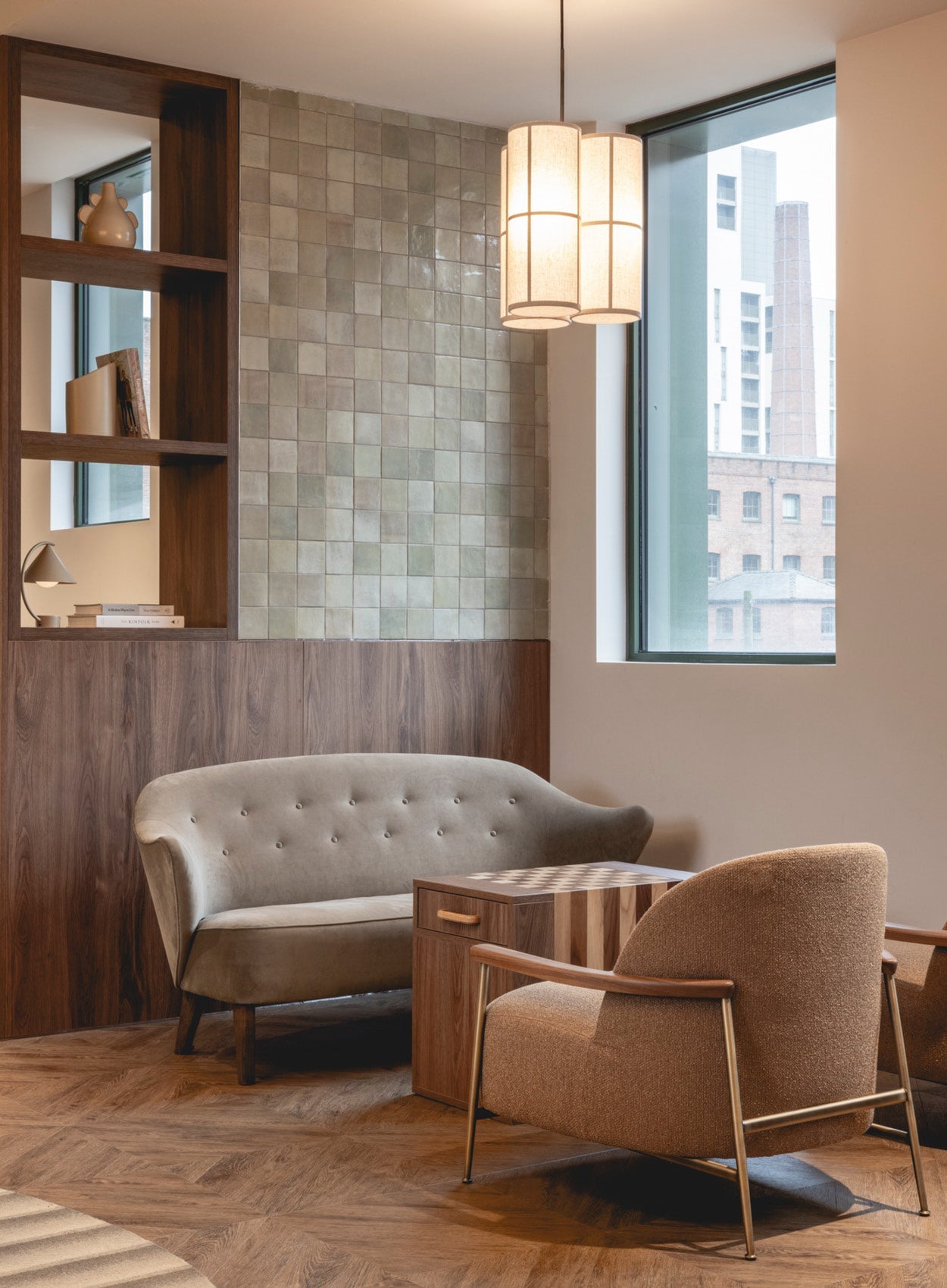 Cozy seating area with taupe tufted loveseat, beige upholstered armchair, wooden side table and cylinder fabric pendant light