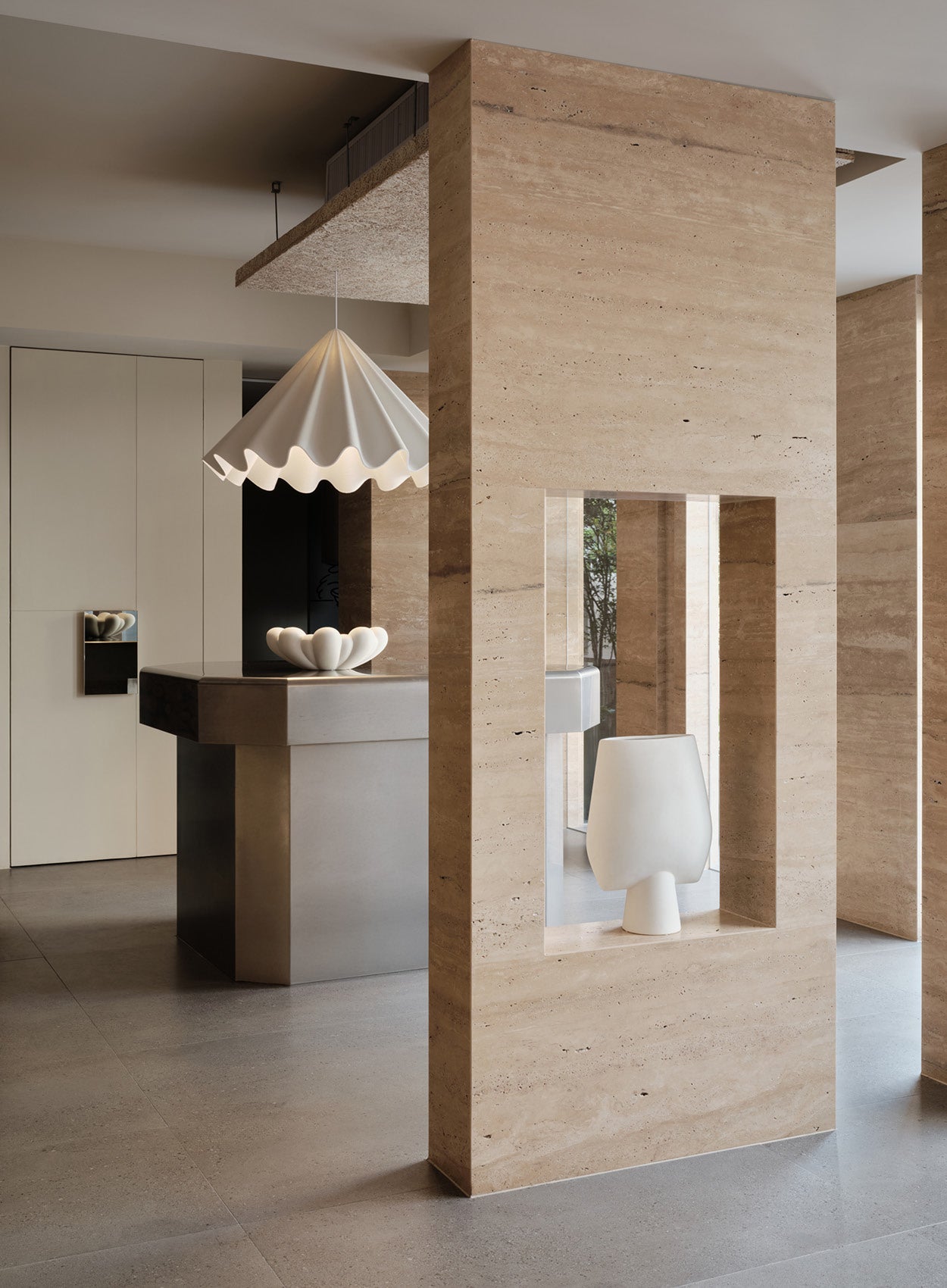 Minimalist interior with beige travertine columns, a white sculptural pendant lamp and matching ceramic bowl on a stone