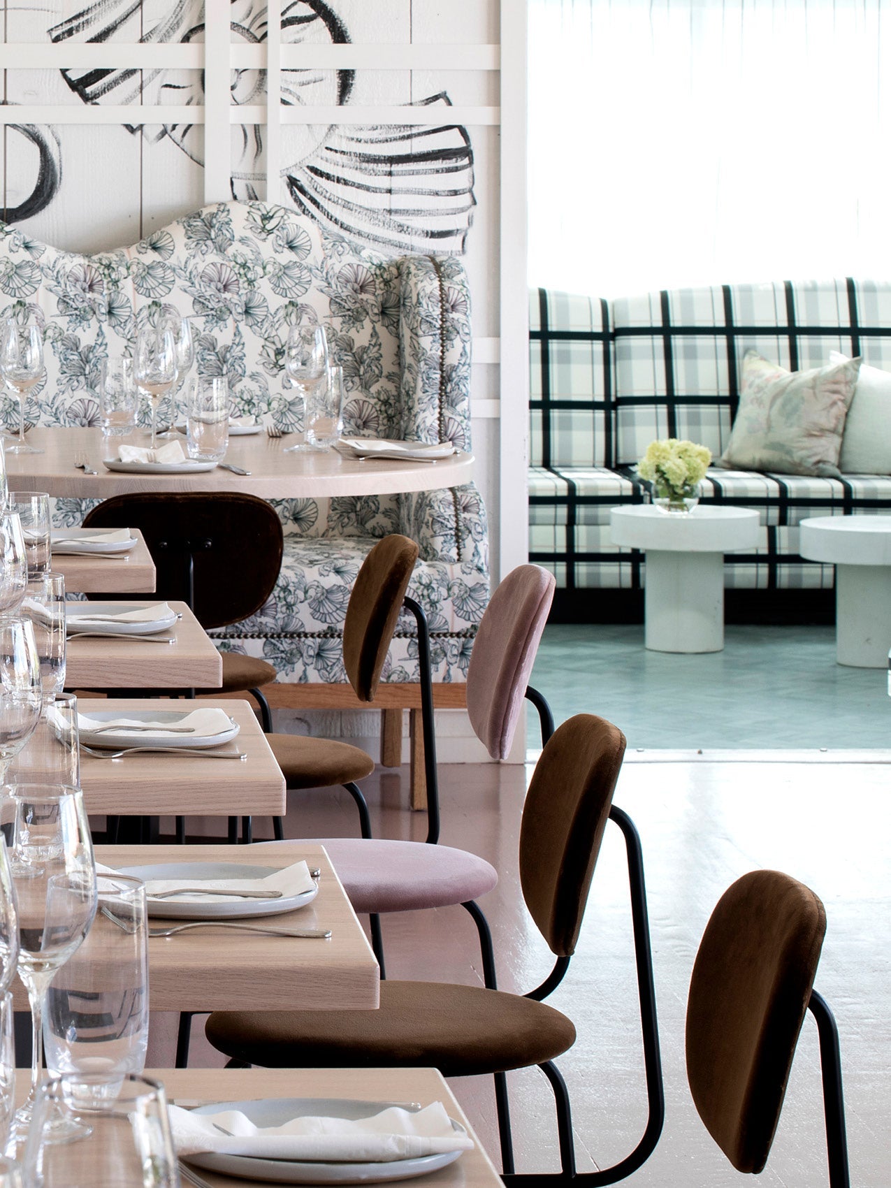 Scandi dining area with light wood tables, brown velvet chairs, patterned floral banquette and plaid sofa in background