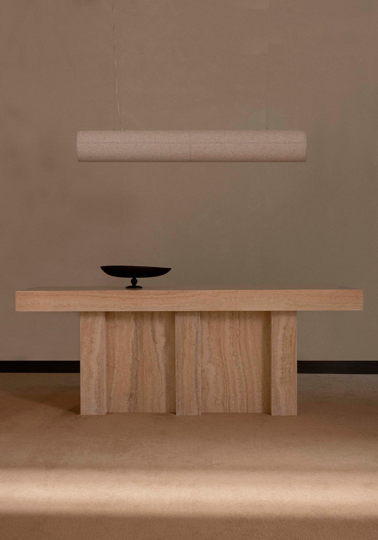 Minimal beige travertine console table with vertical panel legs, black shallow bowl on top and suspended cylindrical fabric