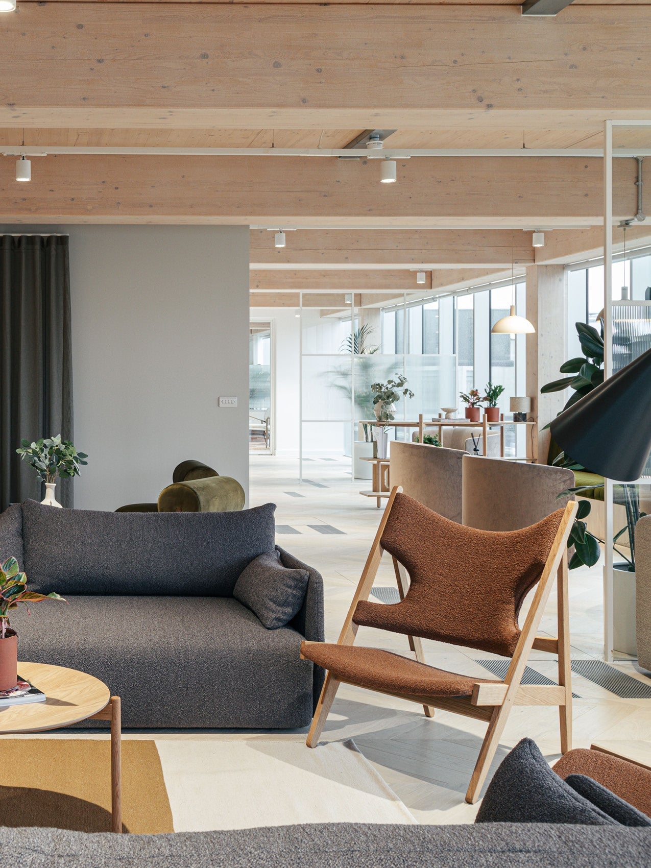 Scandinavian lounge with grey fabric sofa, brown upholstered wooden lounge chair, light wood beams and potted plants