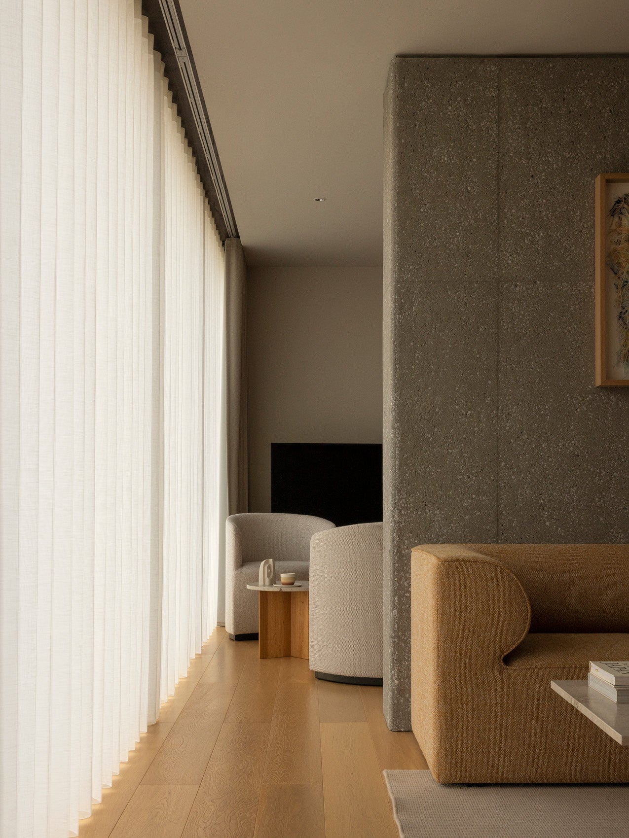 Minimal living room corner with sheer floor-to-ceiling white curtains, beige upholstered armchairs, wooden side table and