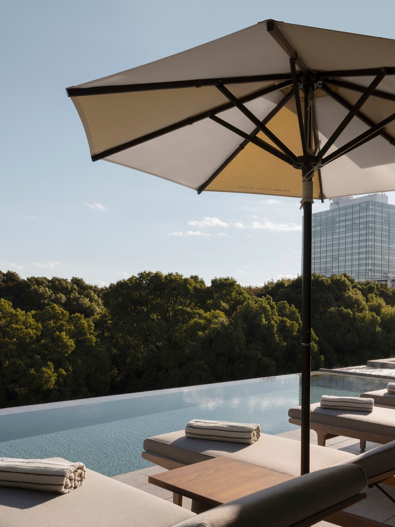 Cream and beige outdoor parasol with black metal frame shading lounge chairs and an infinity pool beside treetops and a