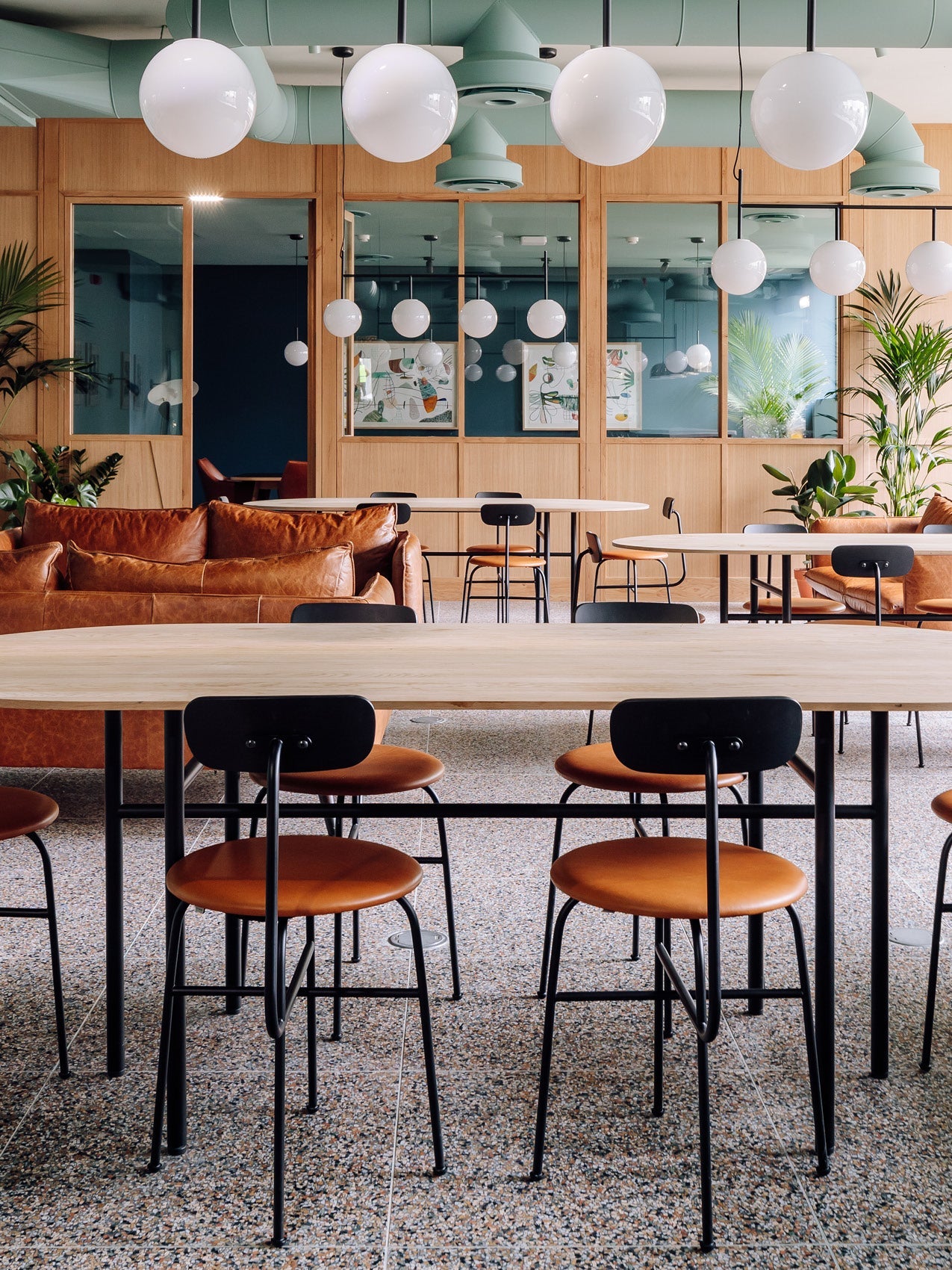 Modern communal lounge with light wood tables, black metal chairs with tan leather seats, brown leather sofas and white