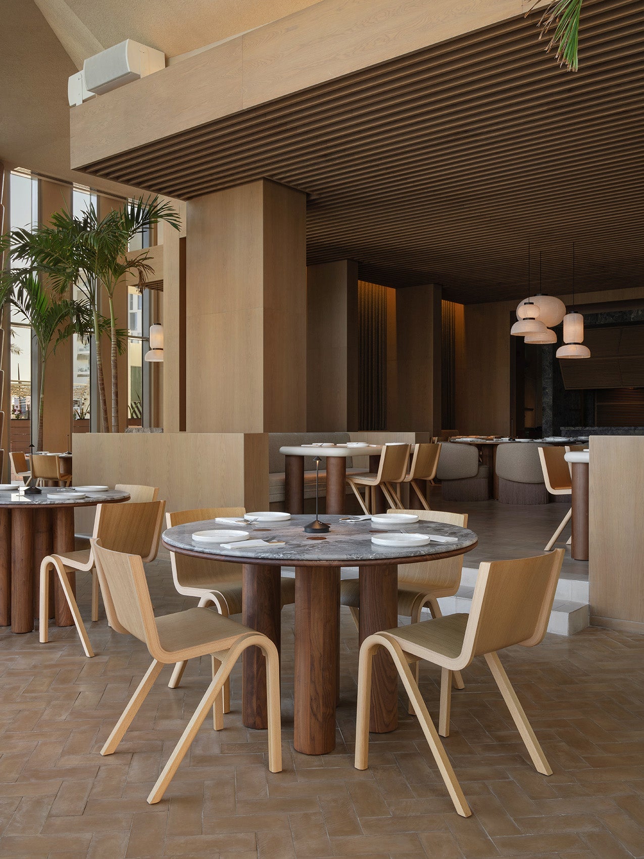Minimal dining space with round dark marble-top table, cylindrical walnut legs and light bentwood chairs in warm oak tones