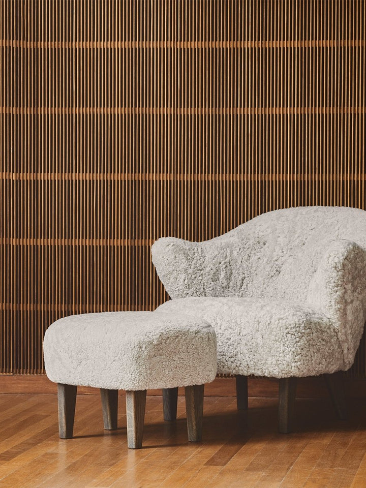 A white sheepskin Ingeborg Lounge Chair and footstool with wooden legs on