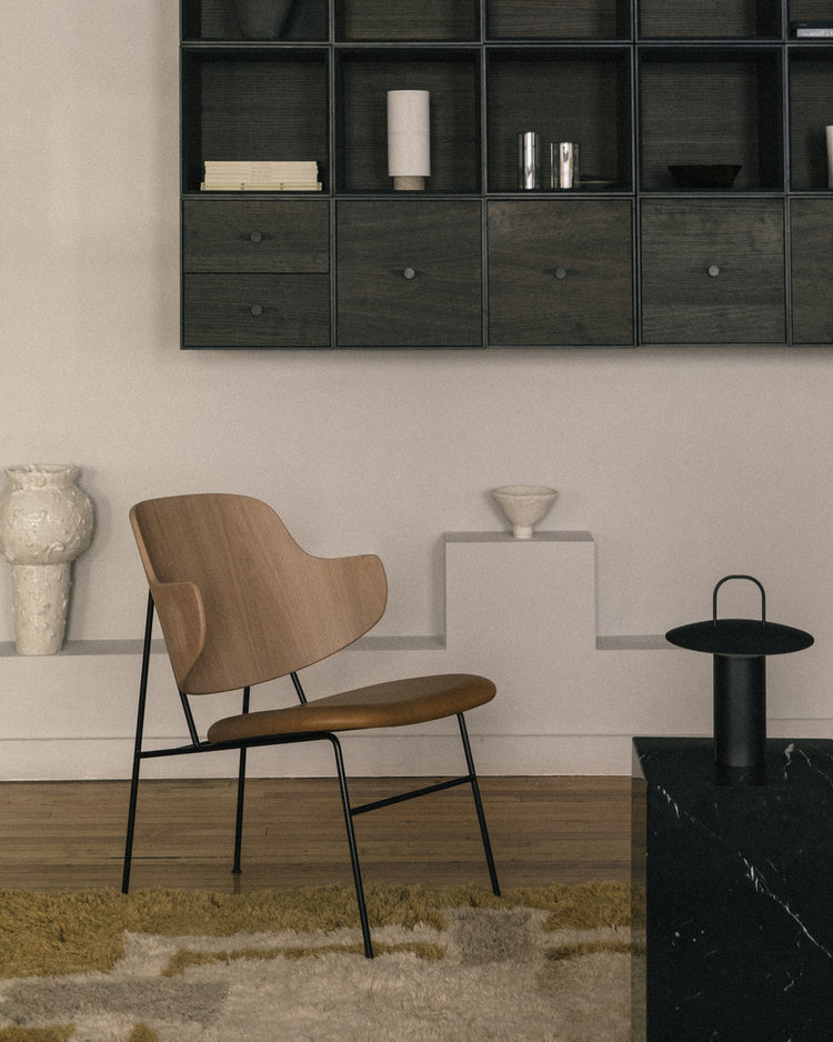 Minimal living room with a wooden lounge chair, black metal legs, floating dark wood cubby shelves and neutral decor