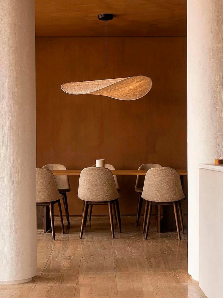 Dining area with curved beige upholstered chairs around a wooden table and an organic-shaped woven pendant light above.