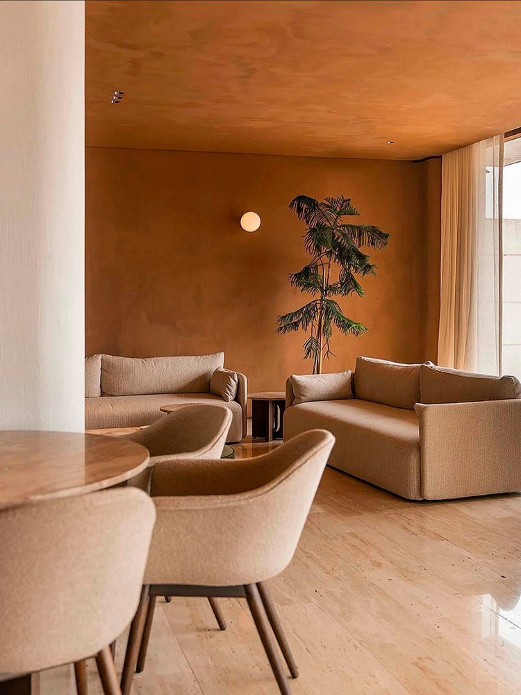 Warm terracotta living room with beige upholstered sofas and armchairs, round wall light and potted palm by sheer curtains
