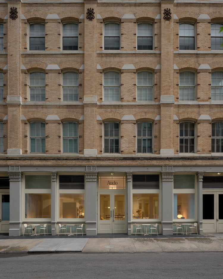 Beige brick building facade with arched windows and ground-floor pale green café entrance, small white tables and chairs