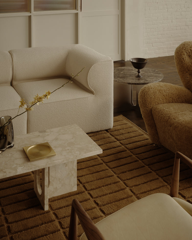 Neutral-toned bouclé sofa and teddy-shearling armchair beside marble side table and textured brown rug.