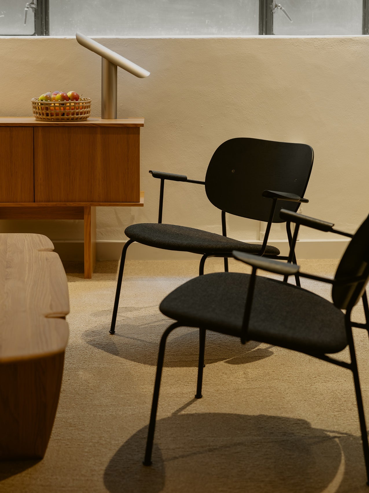 Black minimalist lounge chairs with slim metal legs and curved wooden backs beside a wooden sideboard and modern table lamp