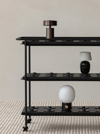 A black Charging Trolley displaying various portable lamps including the Column, Torso, and JWDA, standing on a Houkime Rug.