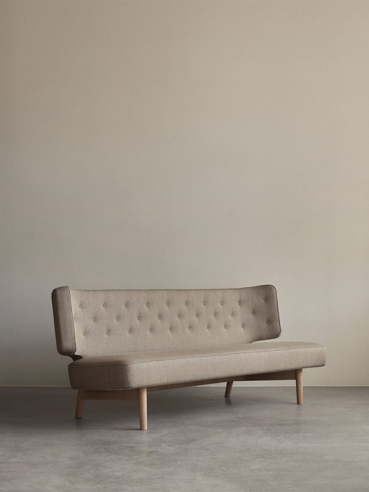 The Radiohus Sofa P2 in beige upholstery with a button-tufted backrest and oak legs, shown in a minimalist room.